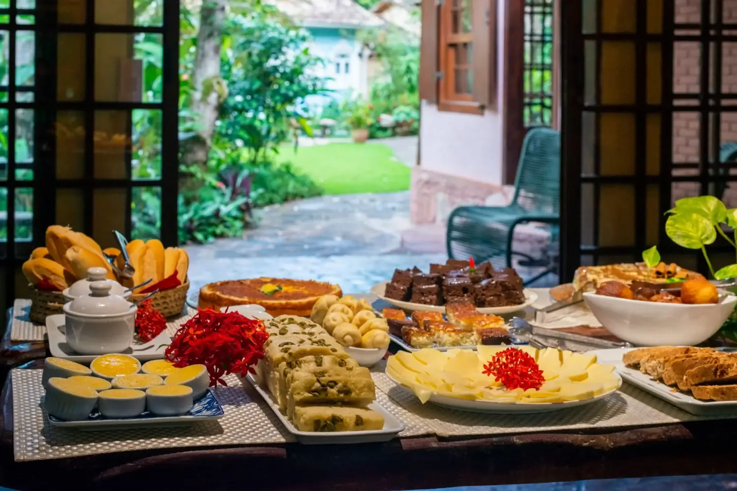 Mesa de café da manhã da Vila Serrano com frutas, pães e vista para o jardim
