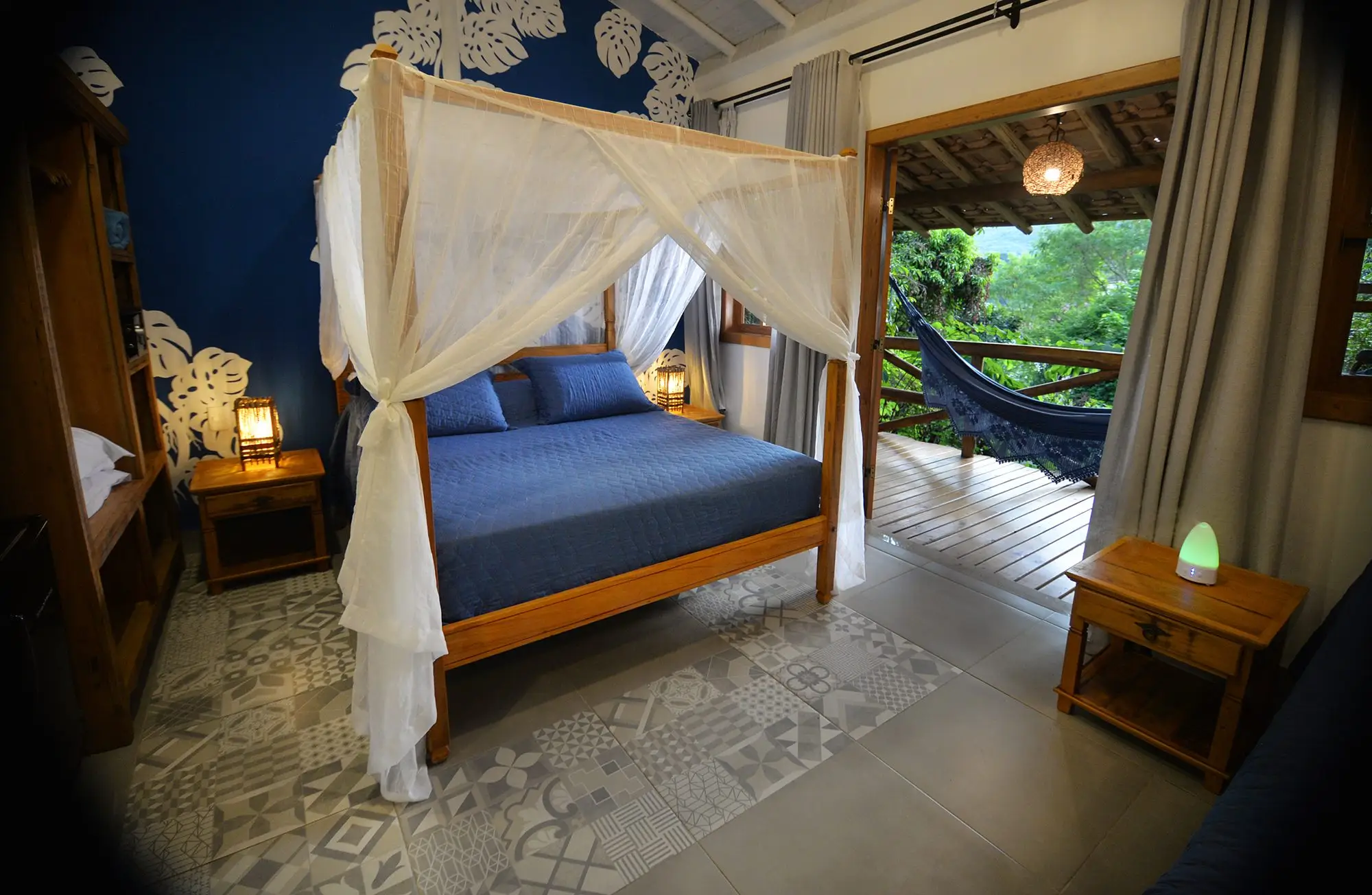 Bangalô com cama de dossel, parede azul e varanda com rede