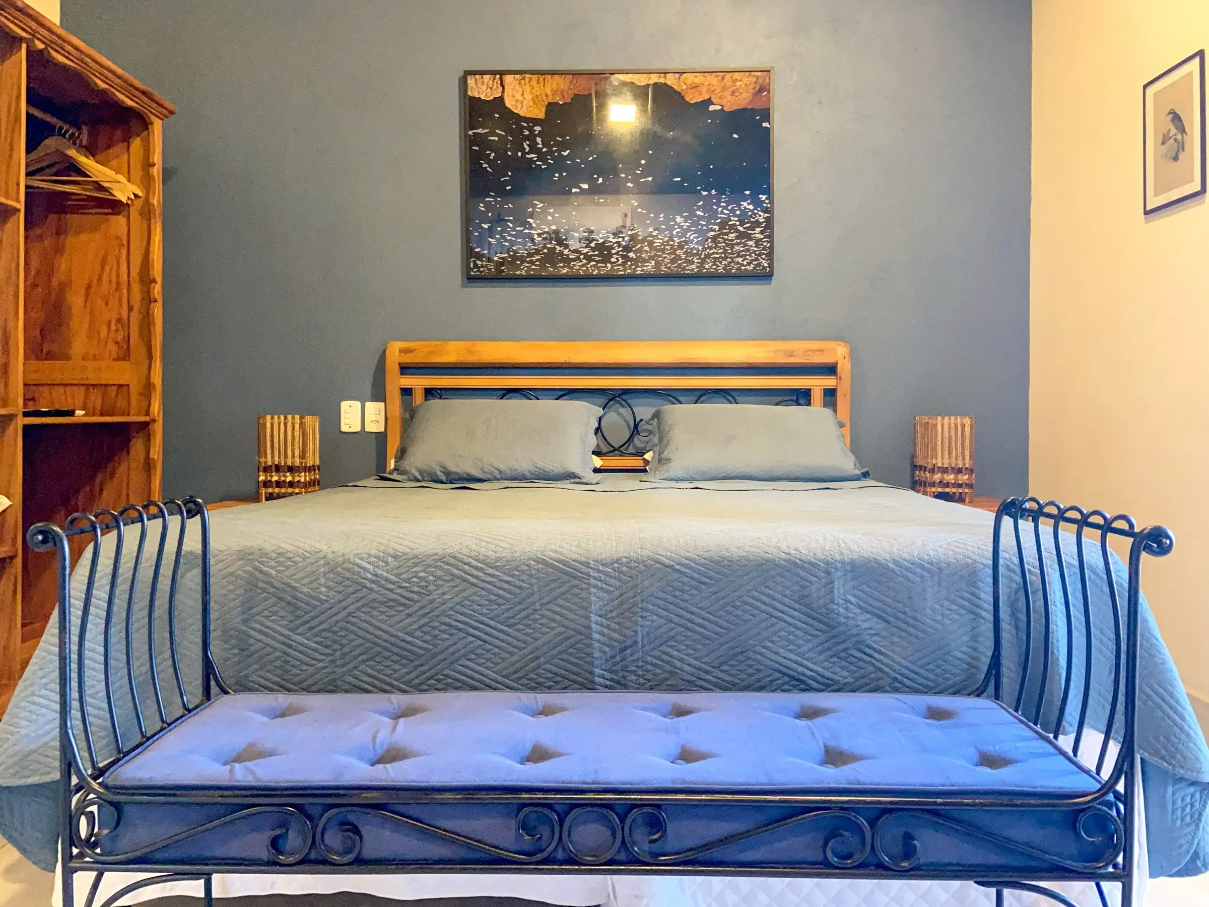 Quarto da Casa Rosa com cama de casal, parede cinza-azulada e banco de ferro