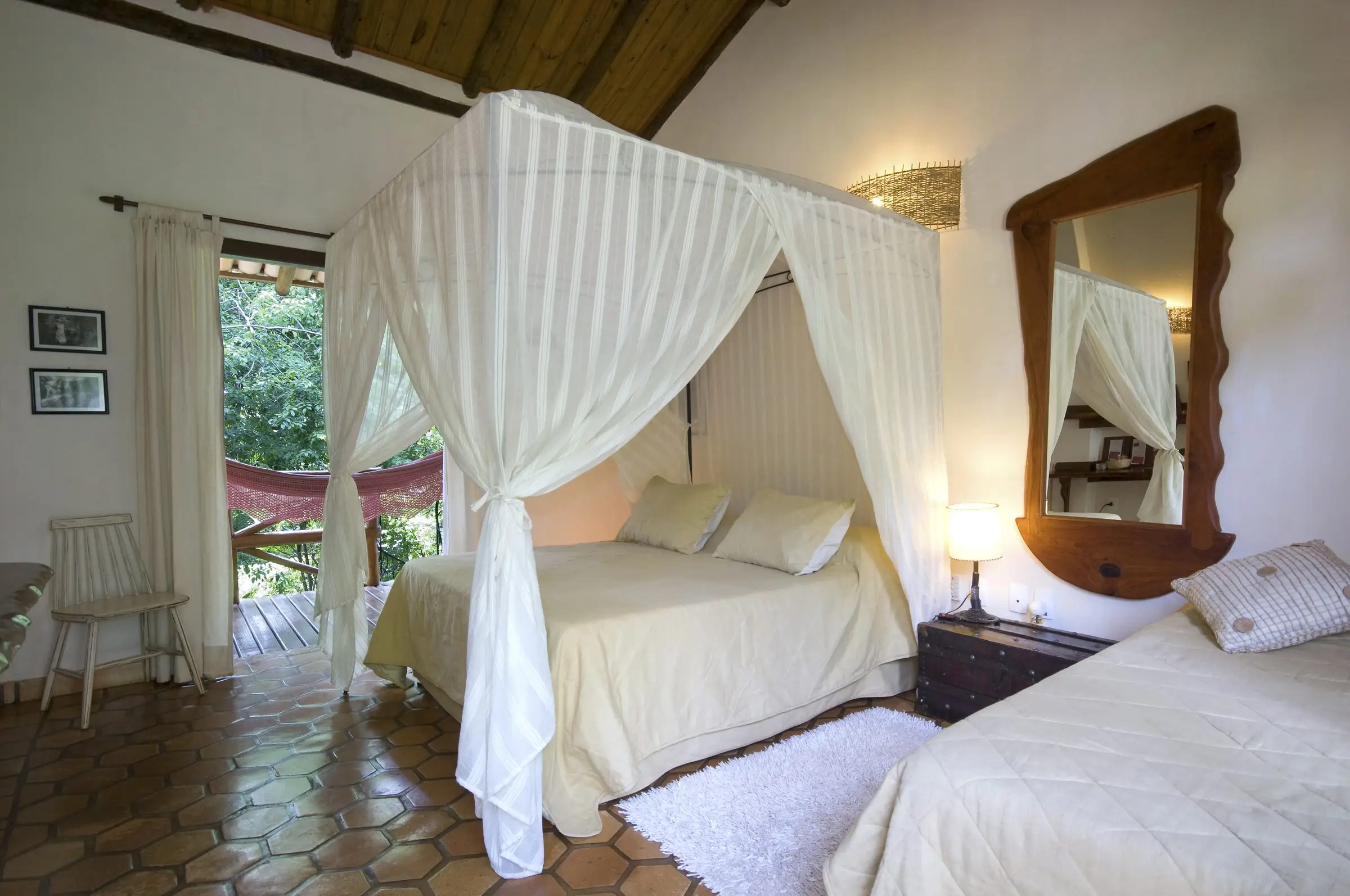 Suíte Vila Jardim com cama de dossel, espelho de madeira e porta para a varanda com rede