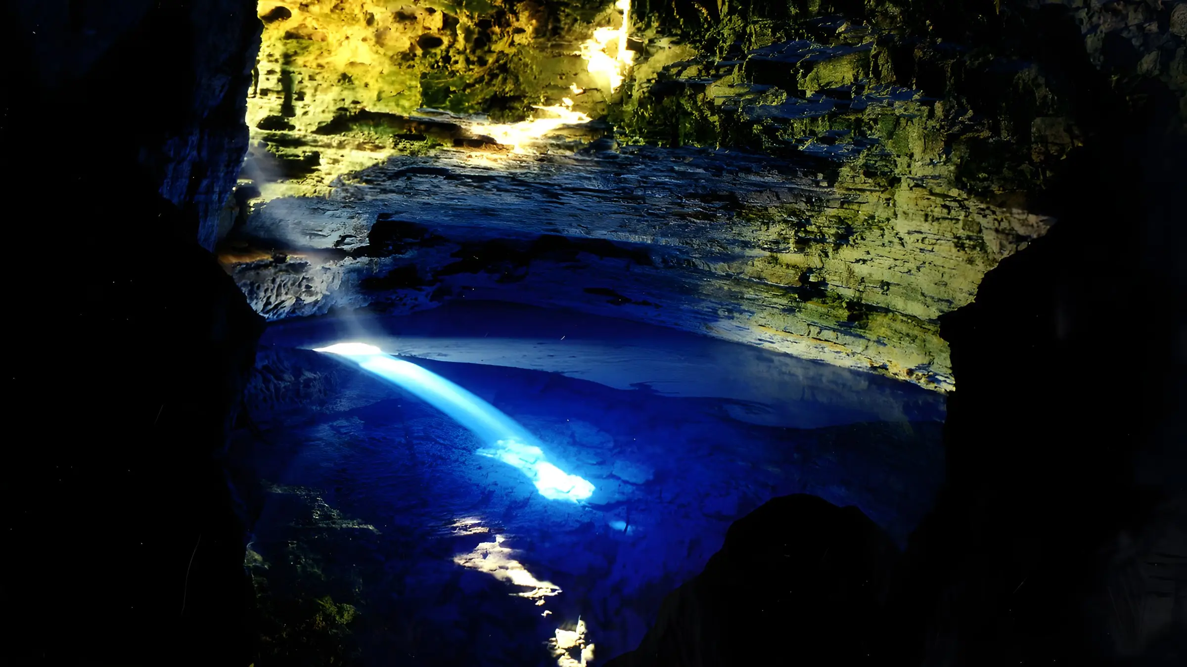 Beam of sunlight lighting the blue water of Poço Encantado inside the cave