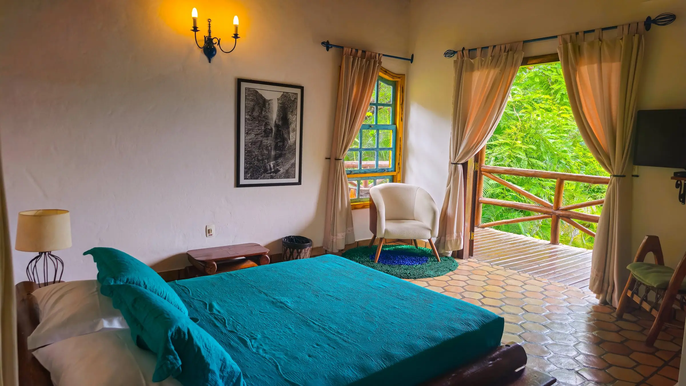 Quarto com colcha turquesa e portas abertas para a varanda com vista do jardim
