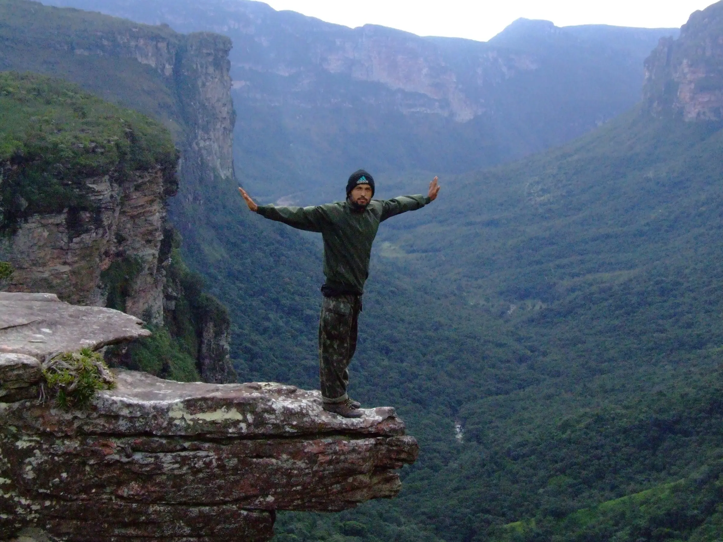 Caminhante de braços abertos sobre uma pedra à beira de um cânion da Chapada Diamantina