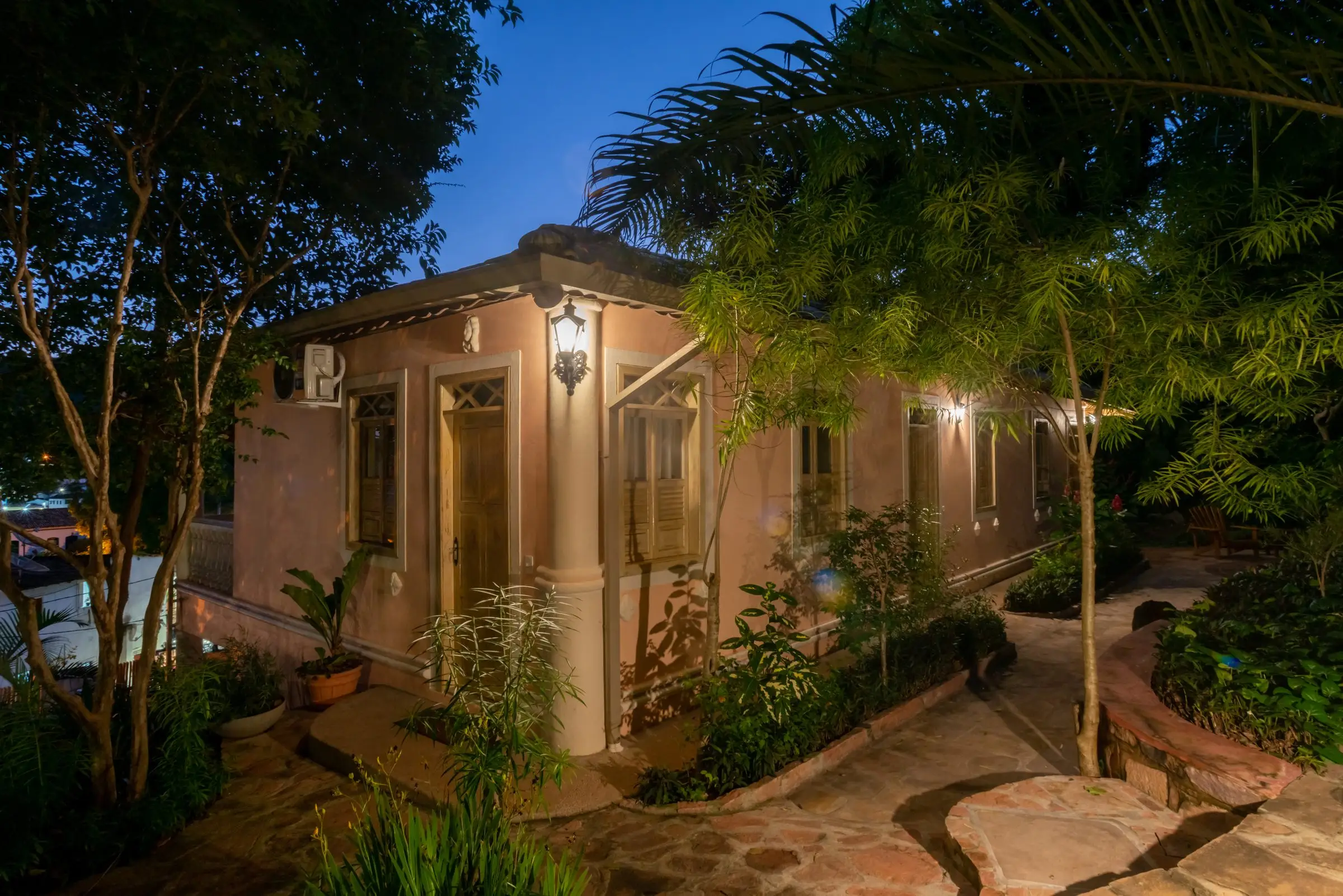 A Vila Serrano house lit at dusk among trees and stone paths