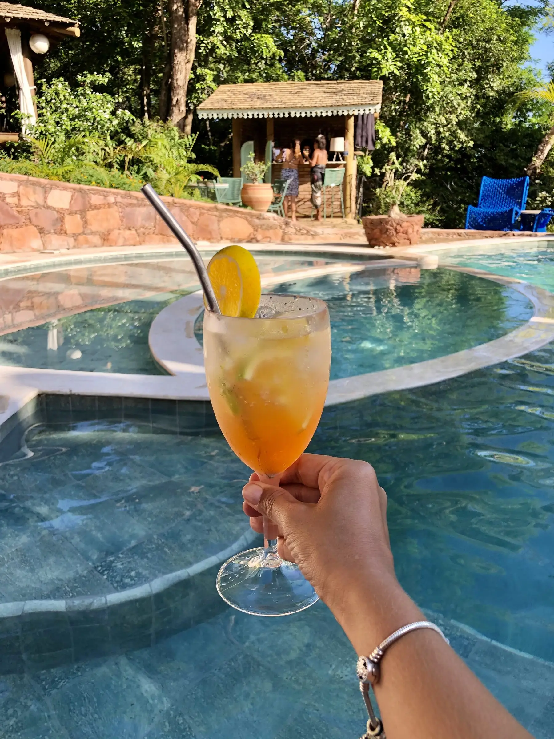 Iced drink with lemon held up over the pool, with the pool bar behind