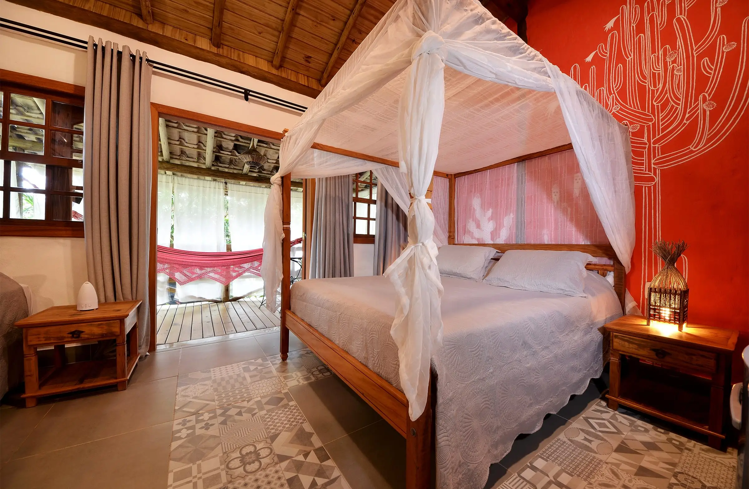 Room with a canopy bed, red wall and doors open to a veranda with a hammock