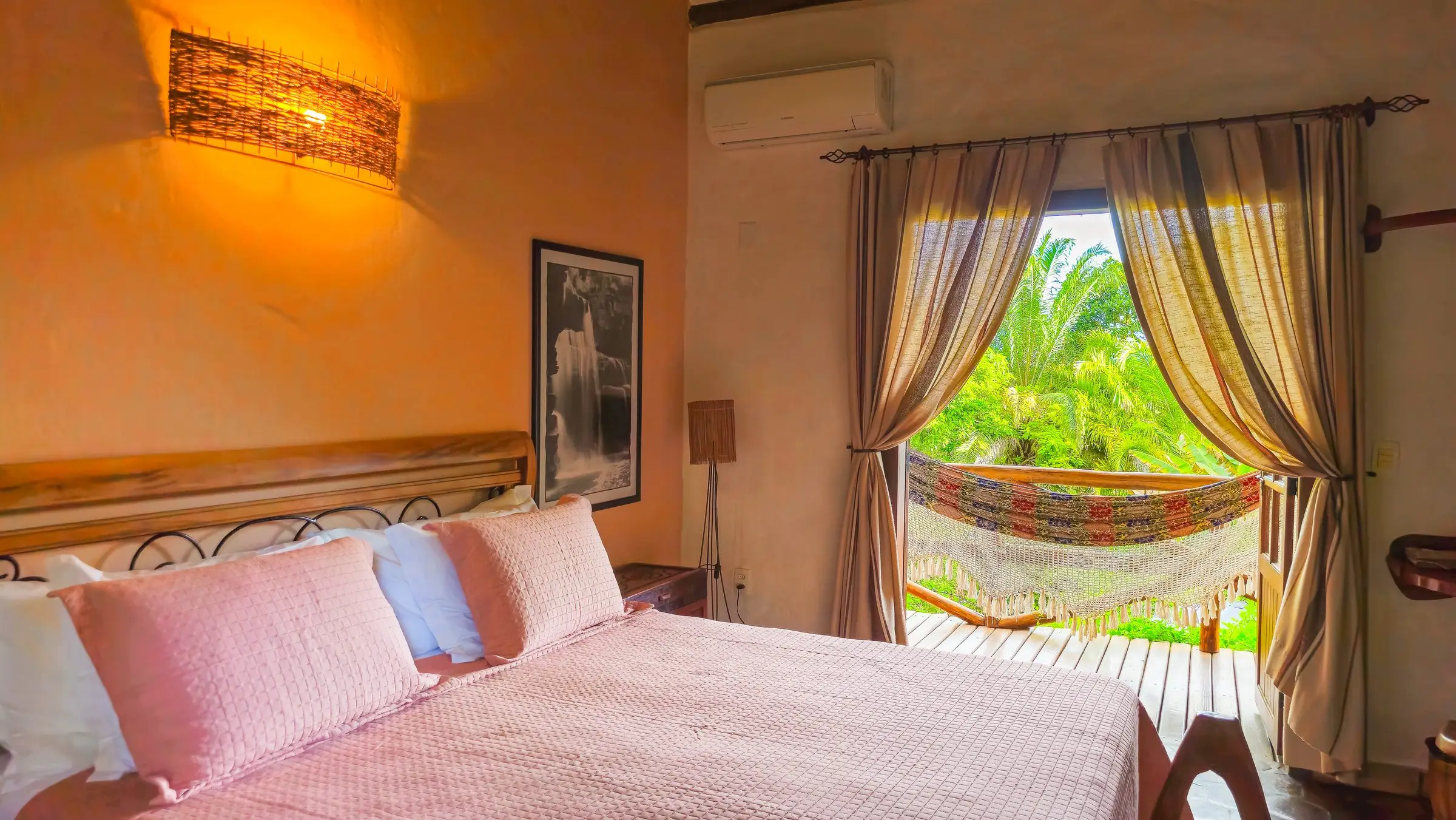 Room with a pink bedspread and doors open to a veranda hammock and the garden