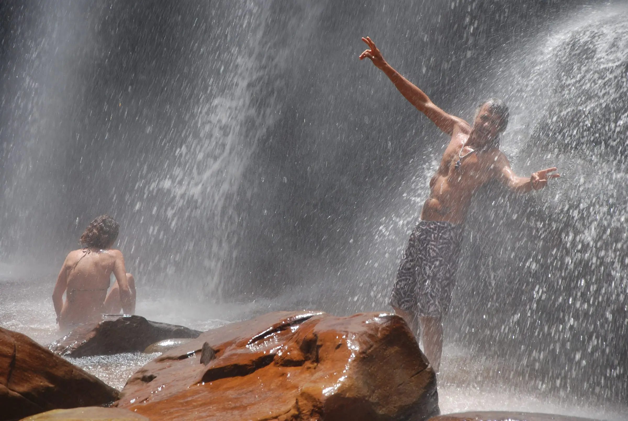 Swimmers beneath a waterfall over reddish rocks in Chapada Diamantina
