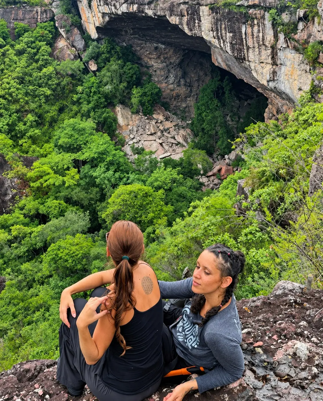 Two people seated on a rocky overlook with the entrance to Gruta do Lapão in the background