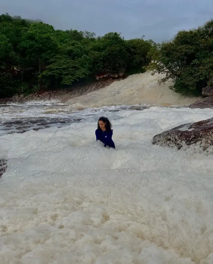 Person in the waters of Ribeirão do Meio, with a cascade and green forest behind